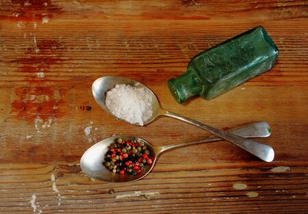 Spoons with coarse salt and peppercorns and glass container on a woooden table