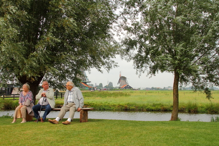 Three senior citizens enjoying a chat while sitting on a bench next to a streamのeditorial素材