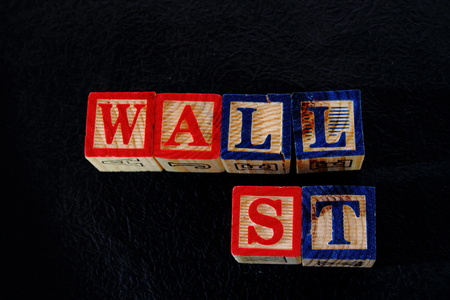 The term wall street displayed visually on a black background using colorful wooden toy blocks in...
