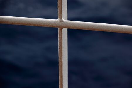 White metal railing shaped like a cross against an out of focus blue background in landscape format...