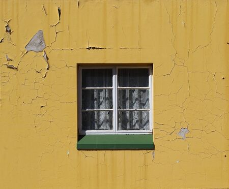 Window with white frames a lace curtain and a green sill in a neglected yellow painted wall in landscape format with copy spaceの写真素材