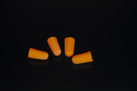 Four orange colored earplugs on a dark background in landscape format with copy space