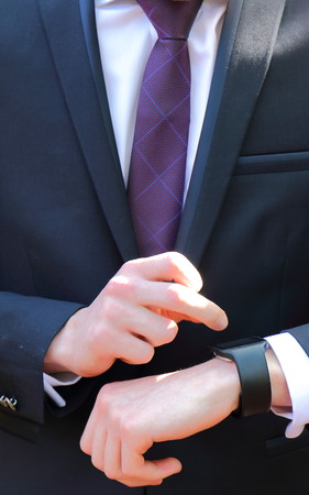 Close-up of a person in a dark suit, a white shirt and a purple tie setting a black watch in portrait format with copy spaceの写真素材