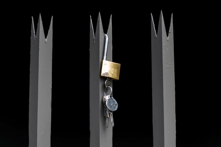 Palisade fence spikes with a lock and keys against a black background, image in landscape format with copy spaceの写真素材