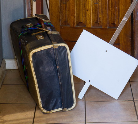 Warn, retro old cardboard suitcase and a blank white placard outside an open doorwayの写真素材