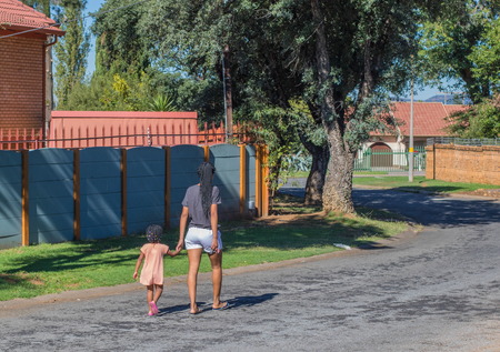 Johannesburg, South Africa - unidentified African mother and child in traditional dreadlocks hairstyles walk down a residential street in the city image with copy space in landscape formatのeditorial素材