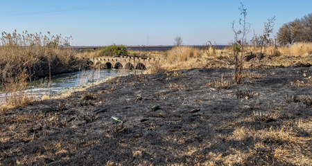 Landscape with black burnt grass, a river and an old concrete low water bridge image with copy space in landscape formatの写真素材