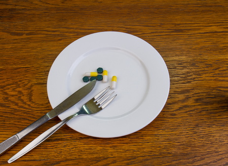 Yellow capsules and green pills on a white plate with a knife and a fork image with copy space in...