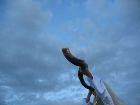A shofar blower dressed in white and gold blowing the shofar against a blue sun set skyの写真素材