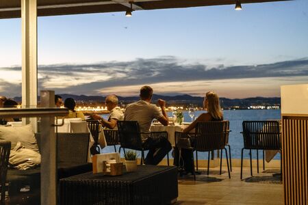 Young couple having dinner at a restaurant by the sea at nightの写真素材