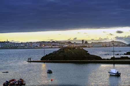 Sunset against the light with the Coruna sky line in the background with people fishing in a small...