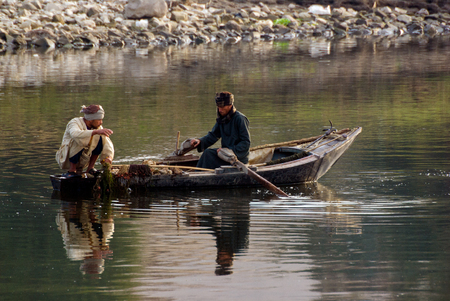 Rio Nilo, near Aswnm, Egypt, February 21, 2017: Two Egyptian fishermen in a small boat fishing, one of them crouched in the stern and the other paddlingのeditorial素材
