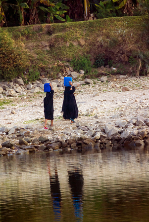 Three Arab women dressed completely in black carrying jerry cans on their heads filled with water from the Nile River in Egypt, near the city of Luxorのeditorial素材
