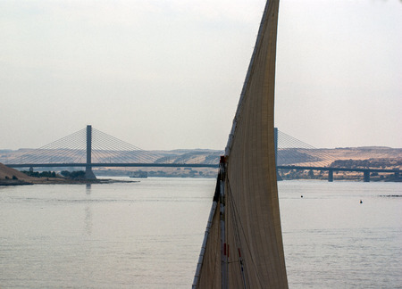 Tip of the mast of a felucca with its sail hoisted and in the background, in contrast, modern bridge over the Nile river, in Egyptの写真素材