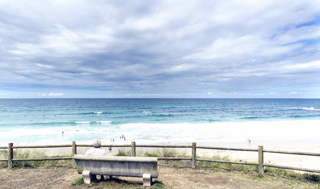 Senior man sitting on a stone bench looking at the atlantic ocean on Razo beach and some people on...