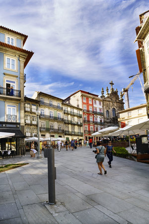 Porto, Portugal. August 12, 2017: Central square of the city with tourists walking and stone floor with many terraces of bars and people walking very old and classic houses of the city and a facade of a baroque church in the backgroundのeditorial素材