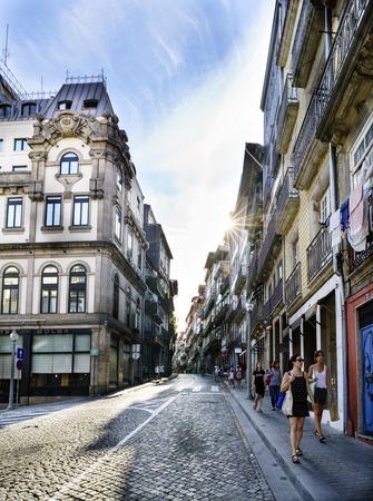 Porto, Portugal. August 12, 2017: Backlight with sun reflections from a downtown street of the cobblestone city and with young people strolling through itのeditorial素材