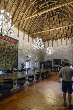 Guimaraes, Portugal. August 14, 2017: Main hall of the palace of the Dukes of Braganza with wooden coffered ceiling, large lamps a large central table with medieval bronze dishes and jugs and granite stone wallsのeditorial素材
