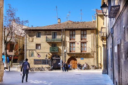 Laguardia, Alava, Spain. March 30, 2018: San Juan square in the center of town with large regular stone blocks and typical medieval houses in the north of Spain, with people walking and sitting on the terrace of a barのeditorial素材