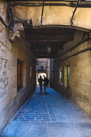 Laguardia, Alava, Spain. March 30, 2018: Narrow cobblestone street under a tunnel formed by medieval style stone houses and people passing through itのeditorial素材