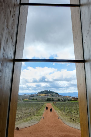 View of the town of Laguardia in Spain from a wooden window in the wine tasting room with people passing through the red dirt road and vineyards on the sidesの写真素材