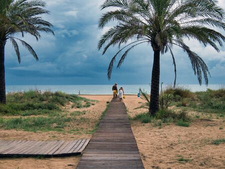 Elderly couple walking on a wooden walkway on the beach of Gandia, Valencia,の写真素材