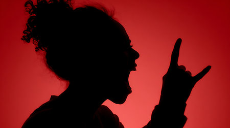 Silhouette of a young woman making a horn gesture on a red backgroundの素材