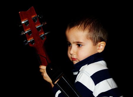 Small boy with guitar acts a rock-n-roll star, isolated on blackの写真素材