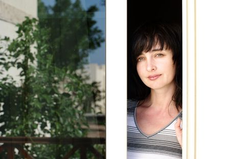 Beautiful brunette woman looking from the balcony with garden reflection in the window