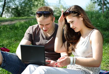 Young couple with laptop in the park on the spring meadowの写真素材