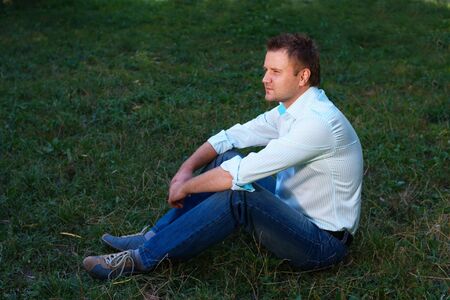 Young man sitting on the grass on summer meadowの写真素材