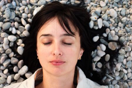 Portrait of woman lie on the stone beach with eyes closedの写真素材