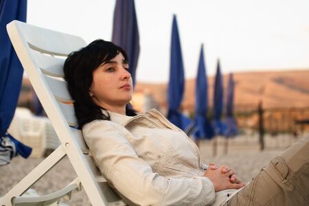 Woman lie in chaise longue on the stone beach in the eveningの写真素材