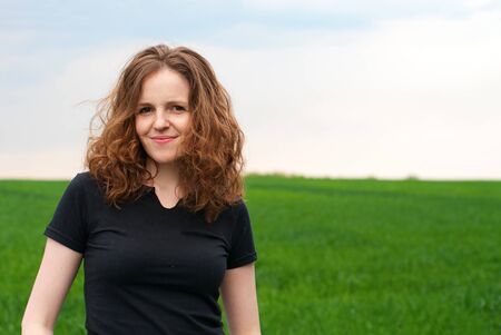 Beautiful redhead curly woman on the green fieldの写真素材