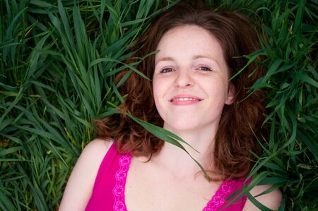 Redhead woman in pink dress lying on the green grass の写真素材