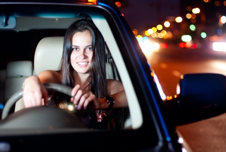 Young smiling woman driving car in the night cityの写真素材