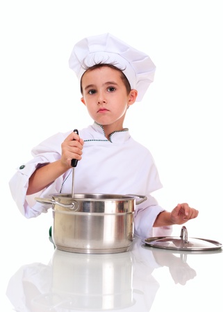 Little boy chef in uniform with ladle stiring in the pot isolated on whiteの写真素材