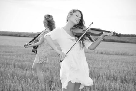 Two young women playing guitar and violin outdoors on the field in summer evening  Grayscale の写真素材