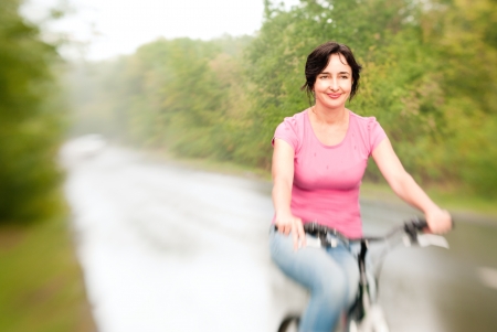 Woman riding bike smiling on the rainy forest road  Lensbaby effectの写真素材