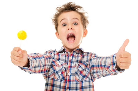Little screaming excited boy shows thumb up with lollipop in hand  isolated on white の写真素材