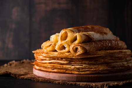 A stack of thin pancakes on a dark wooden background. A traditional dish of crepes for the holiday Maslenitsa. Place for your text, photo for design.の写真素材