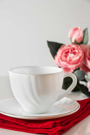 White cup for coffee on a red napkin on a background of pink flowers. Light key, love concept for valentines day.の写真素材