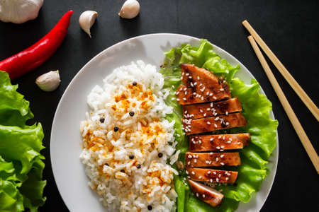Teriyaki chicken with white rice on a plate. Tasty food and Chinese sticks on a dark backgroundの写真素材