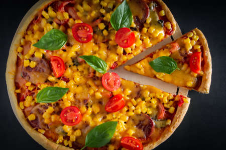 Big italian pizza with tomatoes and basil on a black background. Big pizza with cherry tomatoes, cheese and green basil on a black background. National Italian dish of Mediterranean cuisine. Top view, place for text.の写真素材