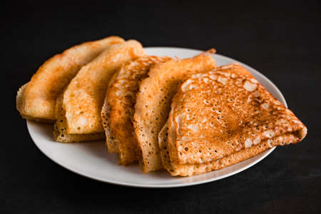 Thin pancakes on a plate on a black background. Traditional Russian food.