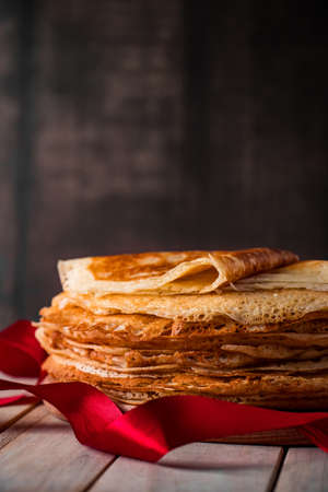 Traditional Russian food - thin pancakes. A stack of crepes on a dark brown wooden background. Vertical photo, place for text.の写真素材