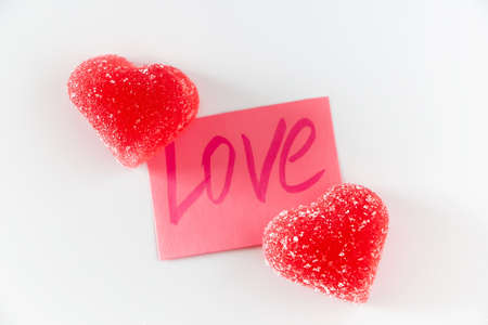 Pink sticker with the word love and two red marmalade in the shape of a heart. Symbol of love on a...