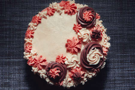 Pink birthday cake with cream flowers on a dark background