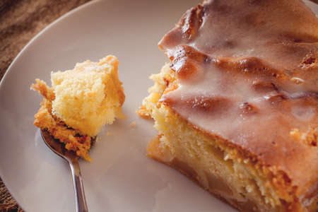 Slice of apple homemade pie on a spoon close-up on a brown background