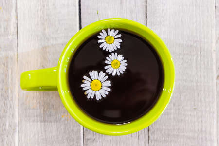 Black tea in a green cup on a wooden background and chamomileの写真素材